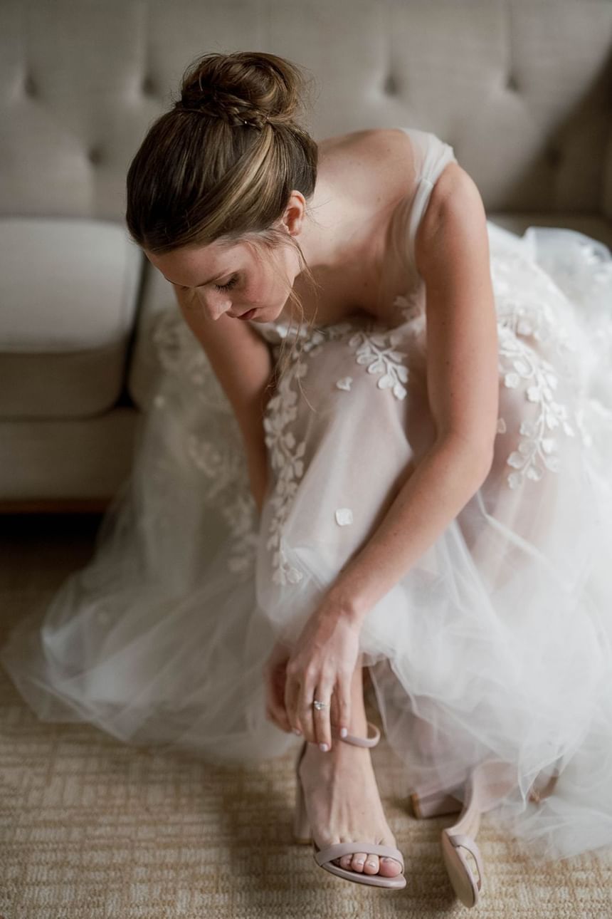 Bride in white gown with lace details putting on strappy heels at The Clifton Hotel in Charlottesville, VA.