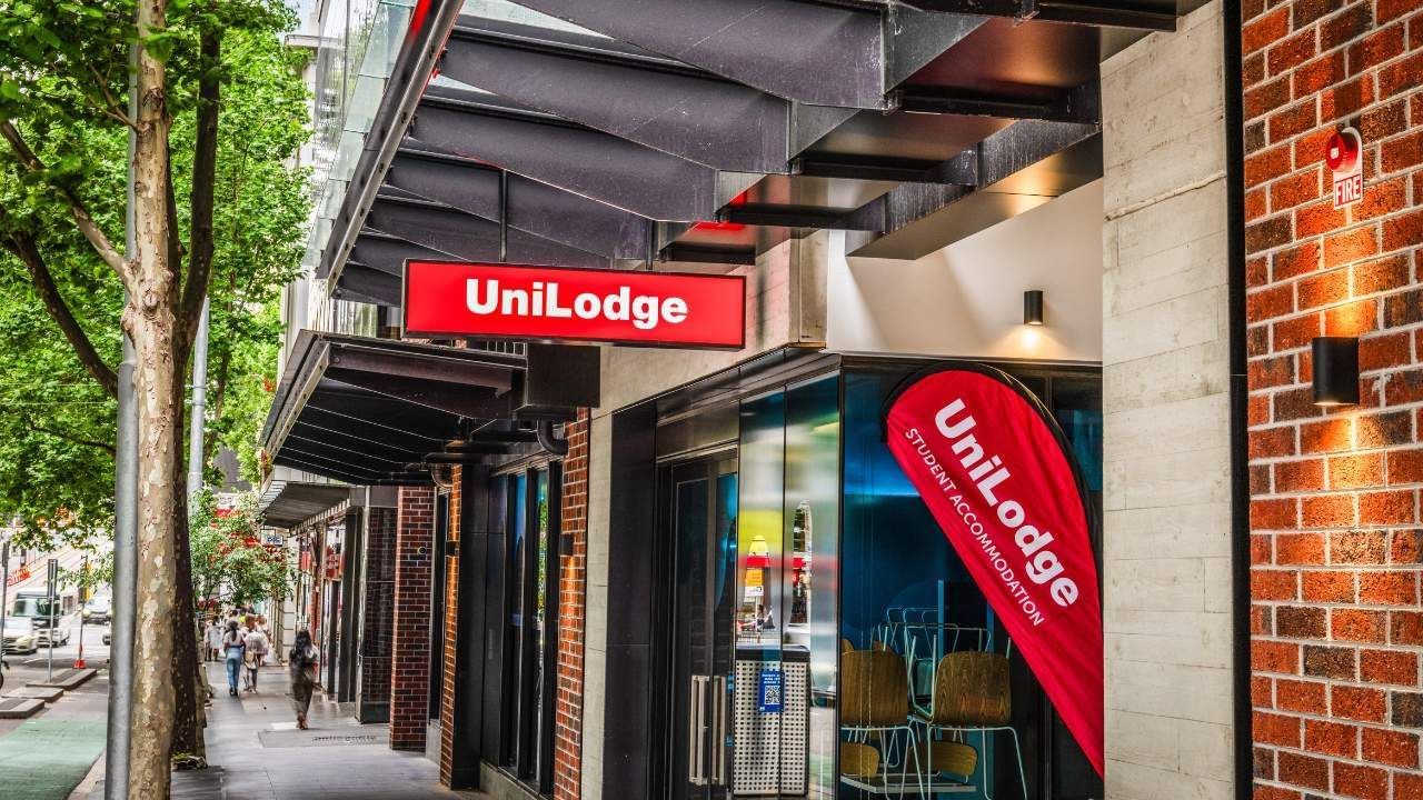 UniLodge building front with red sign and banner, brick walls, and people on sidewalk.