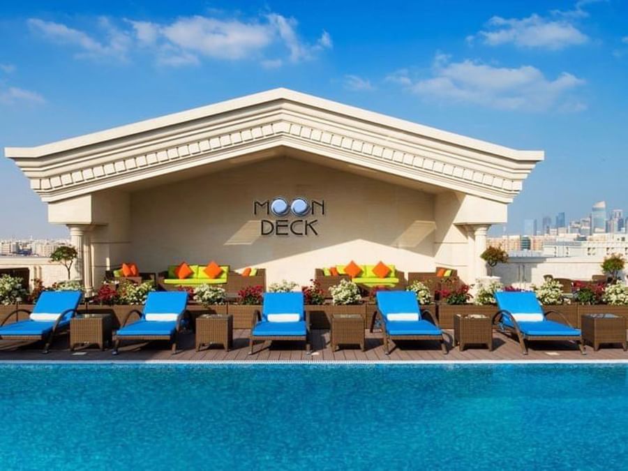 Blue lounge chairs by a pool under the Moon Deck pavilion at a rooftop at Warwick Doha Hotel