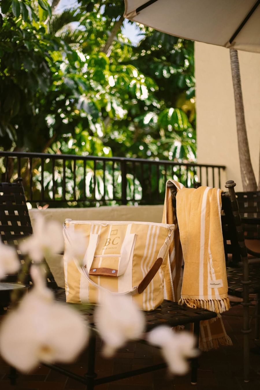 A yellow and white striped bag and towel on a black chair with white flowers in the foreground.