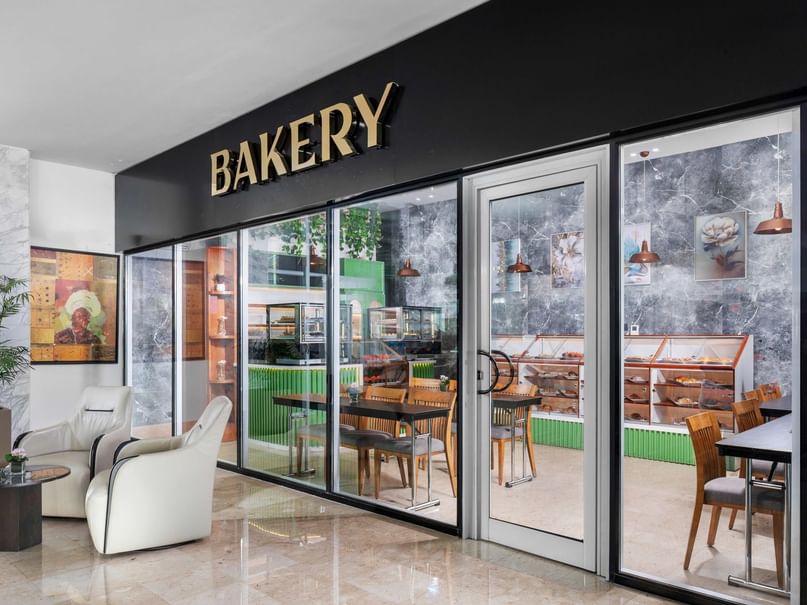 Bakery storefront with glass doors, interior view showing tables, chairs, and display cases with baked goods.