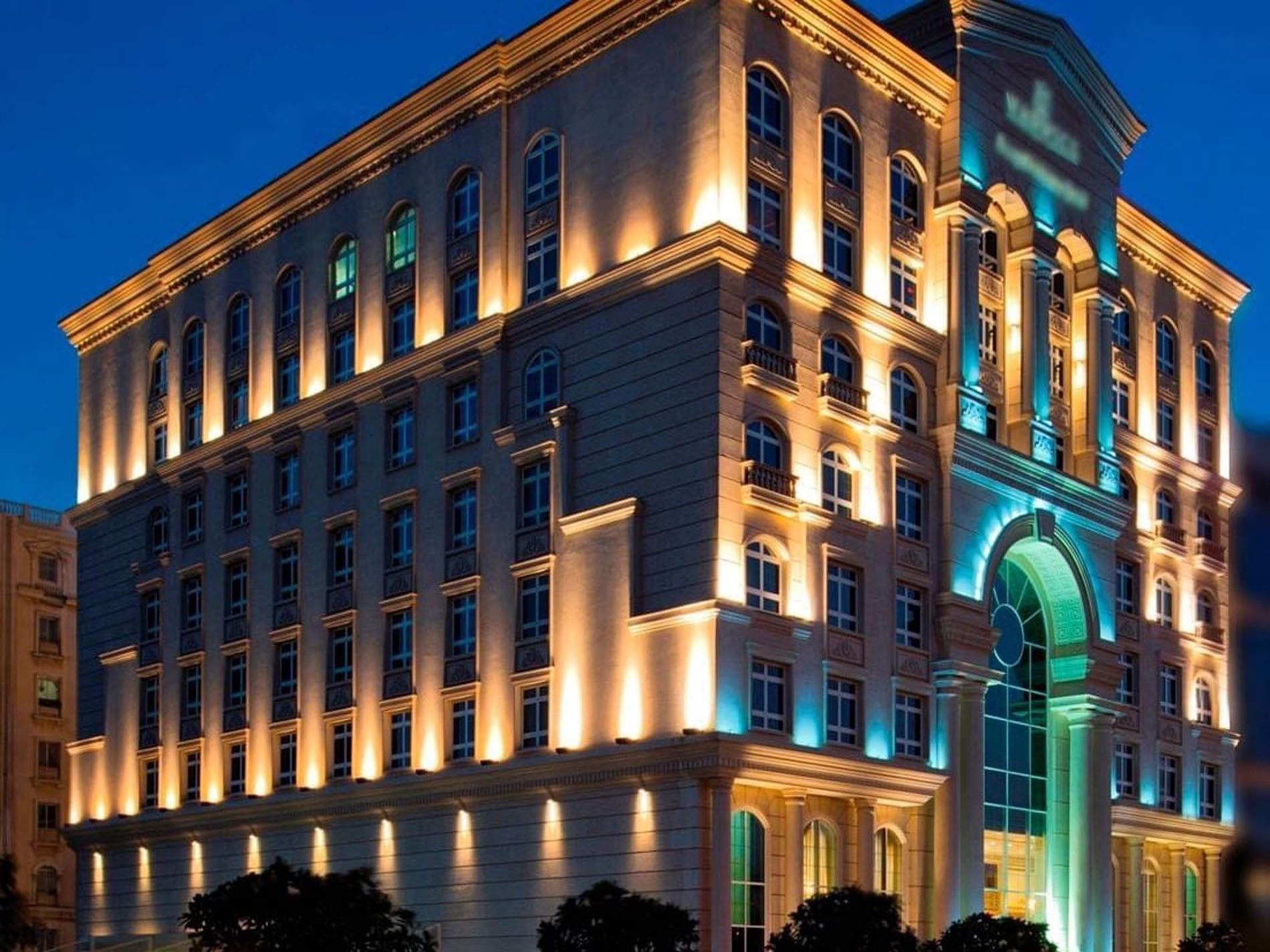 Classic Warwick Doha Hotel exterior with lit windows by a large glass arch at night