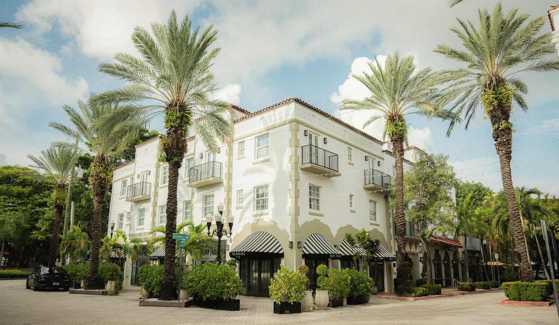 A white, multi-story building with balconies and palm trees in front of it.
