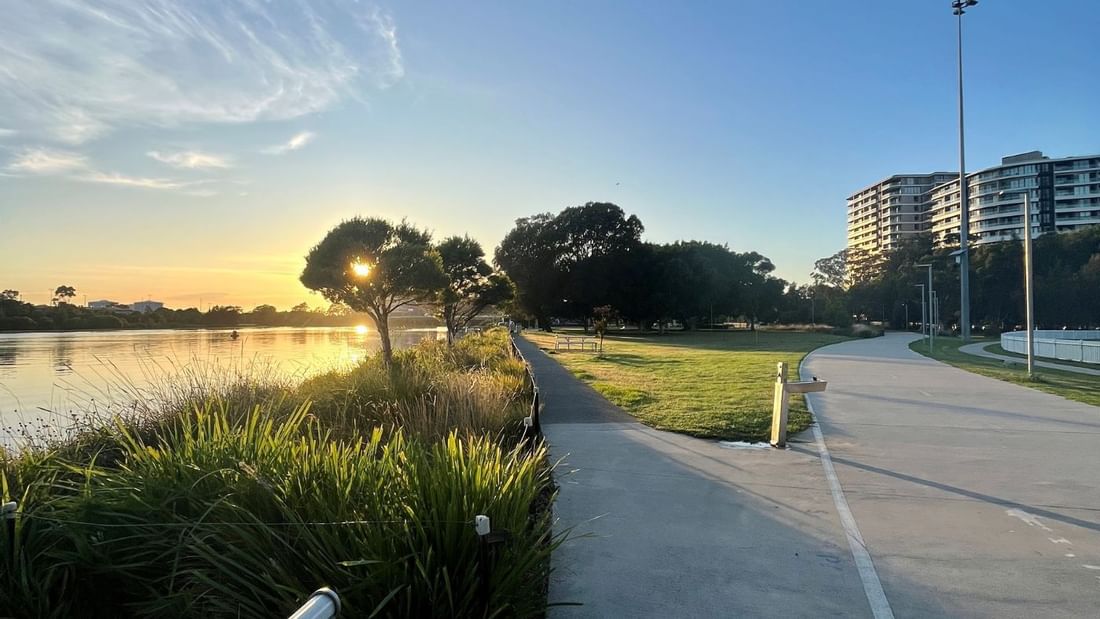 Glowing sunset over Cahill Park with trees, walking path, and skyline views near Novotel Sydney International Airport