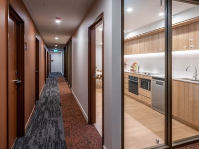 A modern hallway with glass-doored apartments and visible kitchens at UniLodge Brisbane City.