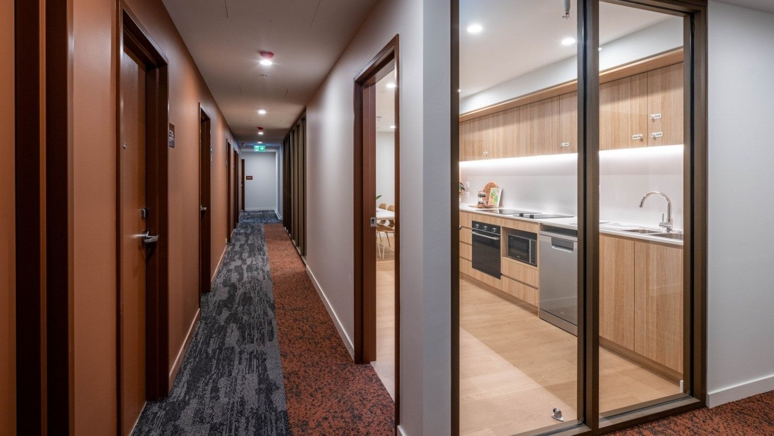 A modern hallway with glass-doored apartments and visible kitchens at UniLodge Brisbane City.