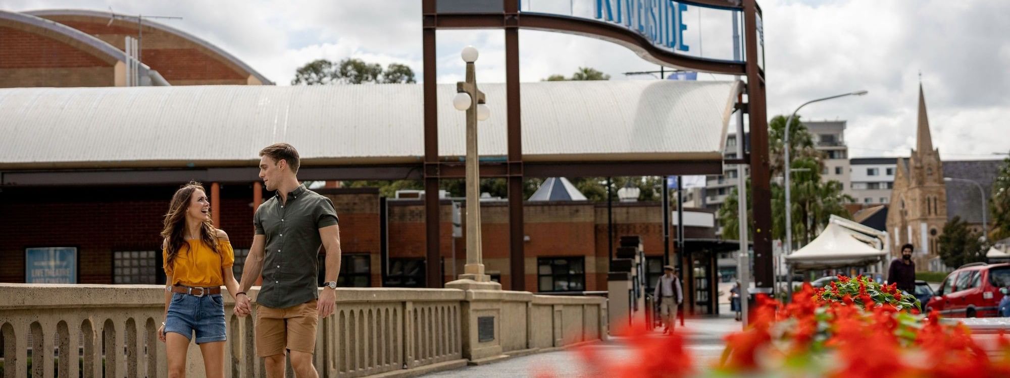 A couple walking hand in hand under a bridge with a sign that says 
