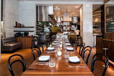 Ciaorigato Restaurant featuring a long wooden dining table and an open kitchen with chefs preparing food at Hotel Bijou