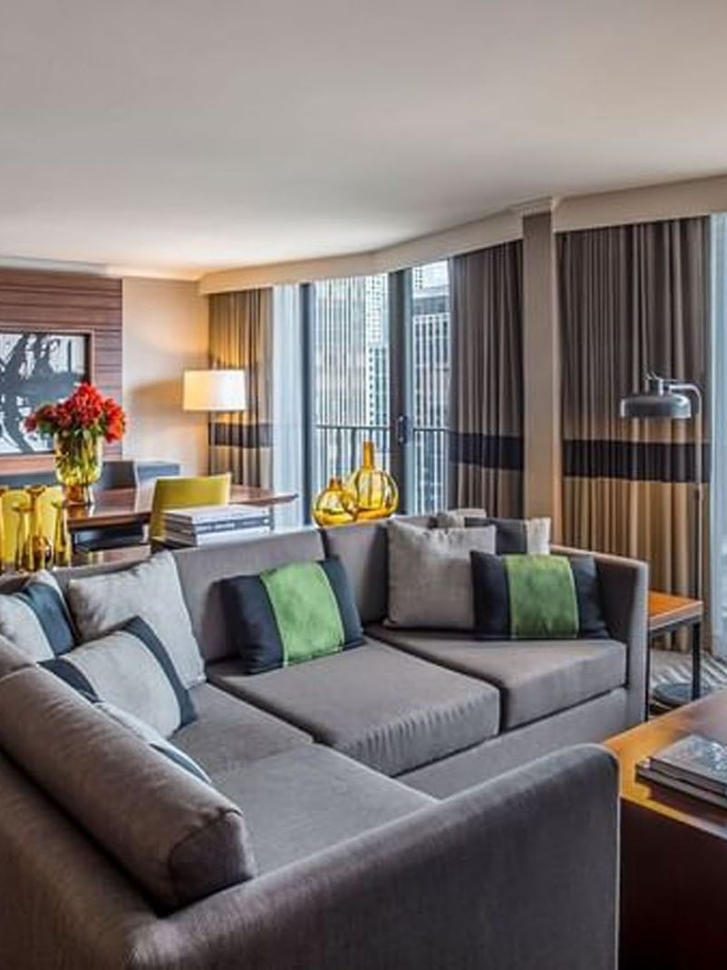 Emerald Suite with a large grey sectional sofa, a wooden coffee table, and city skyline window views at Warwick Seattle