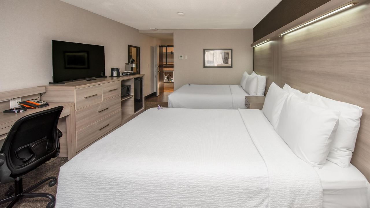 Modern guest room with two queen beds, wood-tone furnishings, wall-mounted TV, and work desk at Coast Calgary University Area Hotel by APA