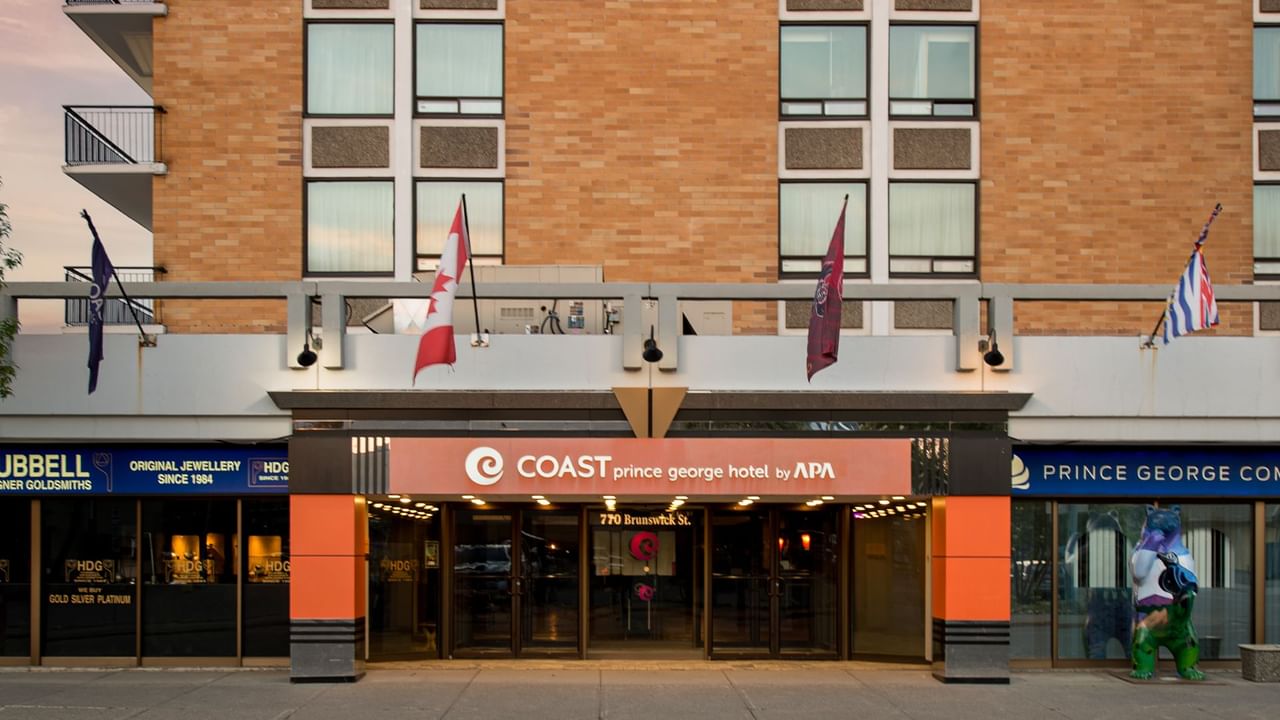 Exterior view of Coast Prince George Hotel by APA with flags and storefronts visible.