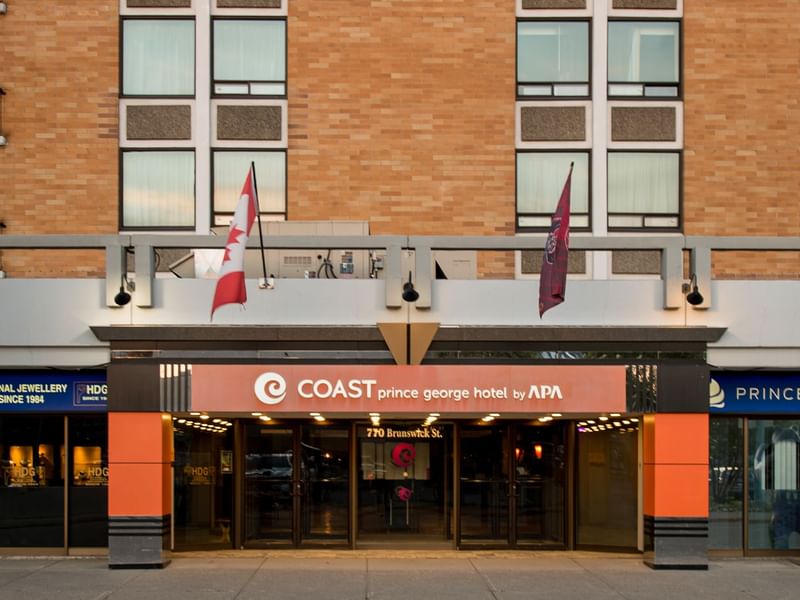 Exterior view of Coast Prince George Hotel by APA with flags and storefronts visible.