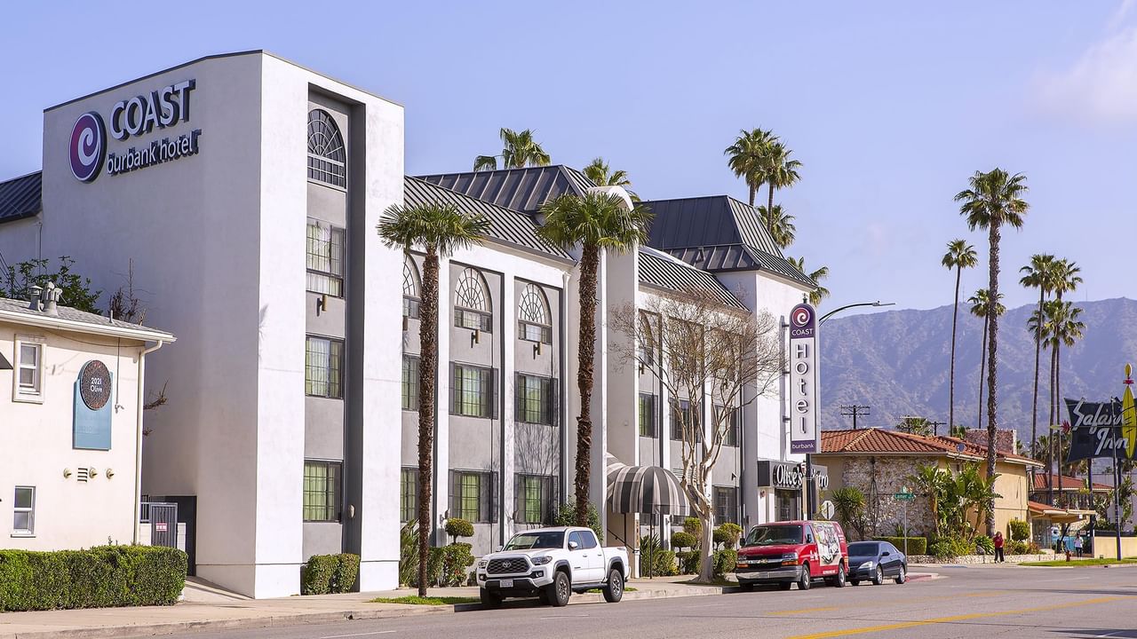Exterior of Coast Burbank Hotel with palm trees and mountains in the background.