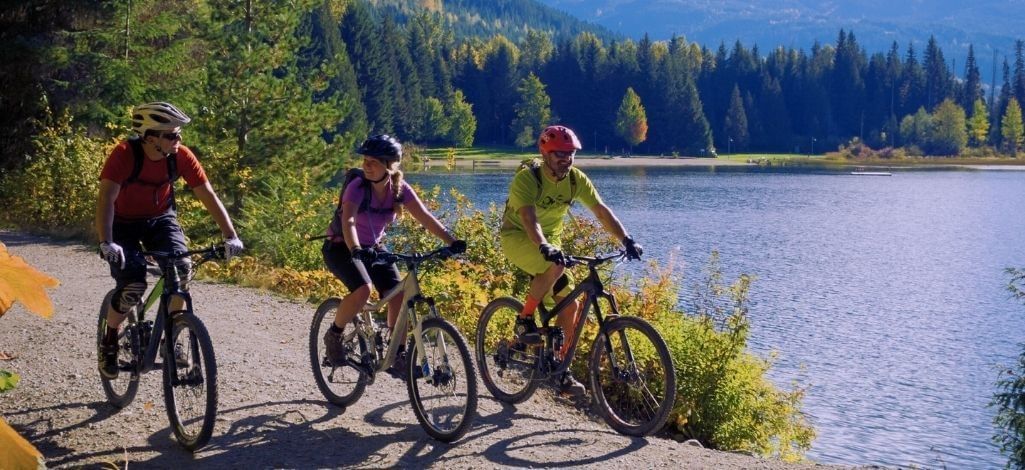 Cyclists riding along a lakeside trail in Whistler surrounded by autumn colors, showcasing outdoor biking and fall adventures in BC.
