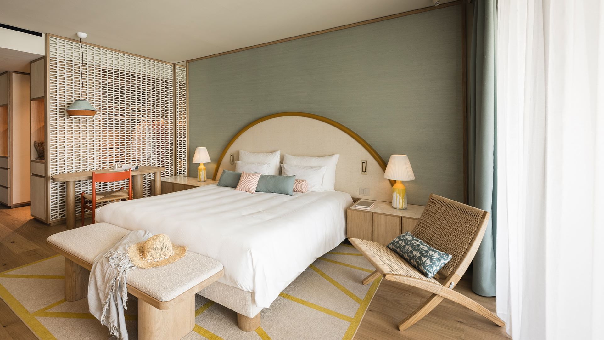 A hotel room with a large bed, nightstands, lamps, chairs, and a rug on the wooden floor.