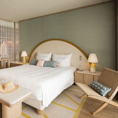 A modern hotel room with a large bed, two chairs, and wooden flooring.