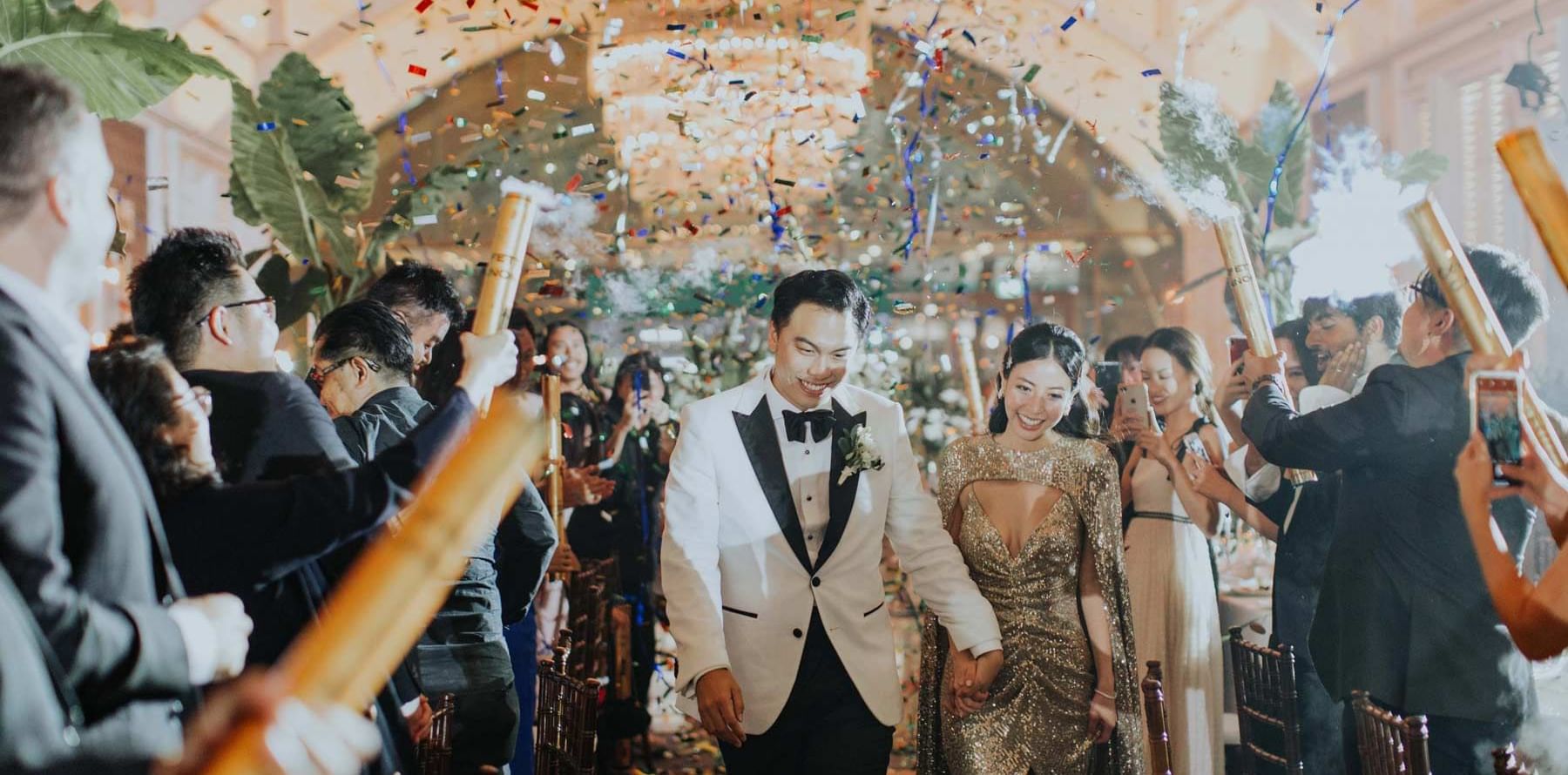 Confetti rains down on while married couple walking through reception at The Fullerton Hotels and Resorts