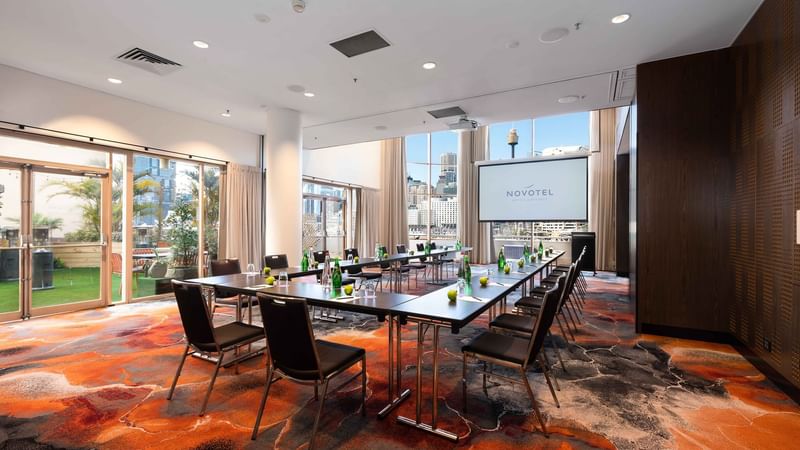 U-shape table set up facing the projector screen in The Hunter Room 2 at Novotel Sydney on Darling Harbour