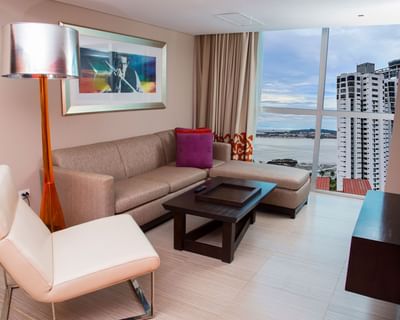 Sectional sofa & coffee table by floor-to-ceiling windows with a bay view in Suite Gold City View at Megapolis Hotel Panama