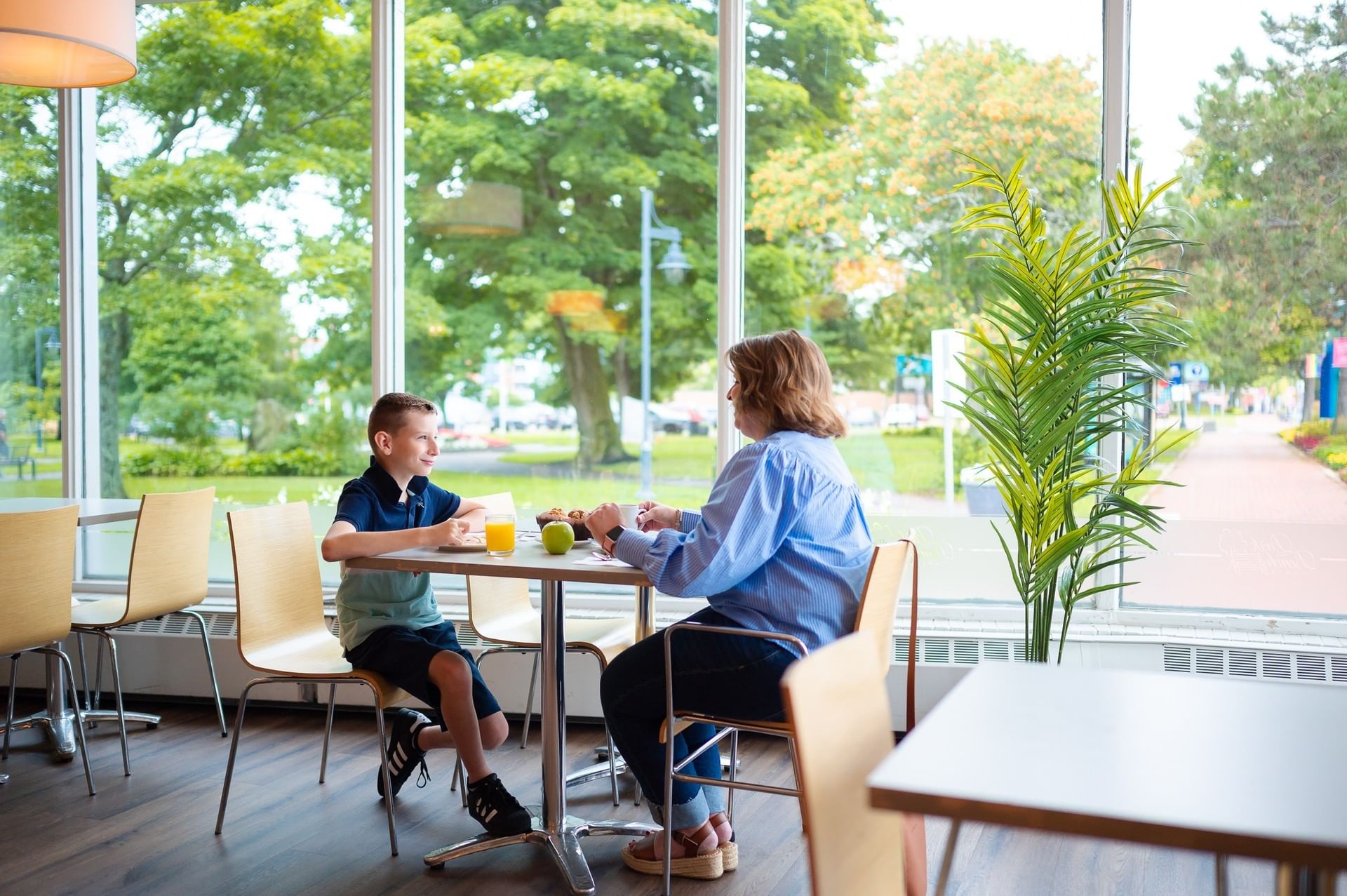Woman and young boy enjoying breakfast by a large glass window overlooking lush green trees at Rodd Moncton