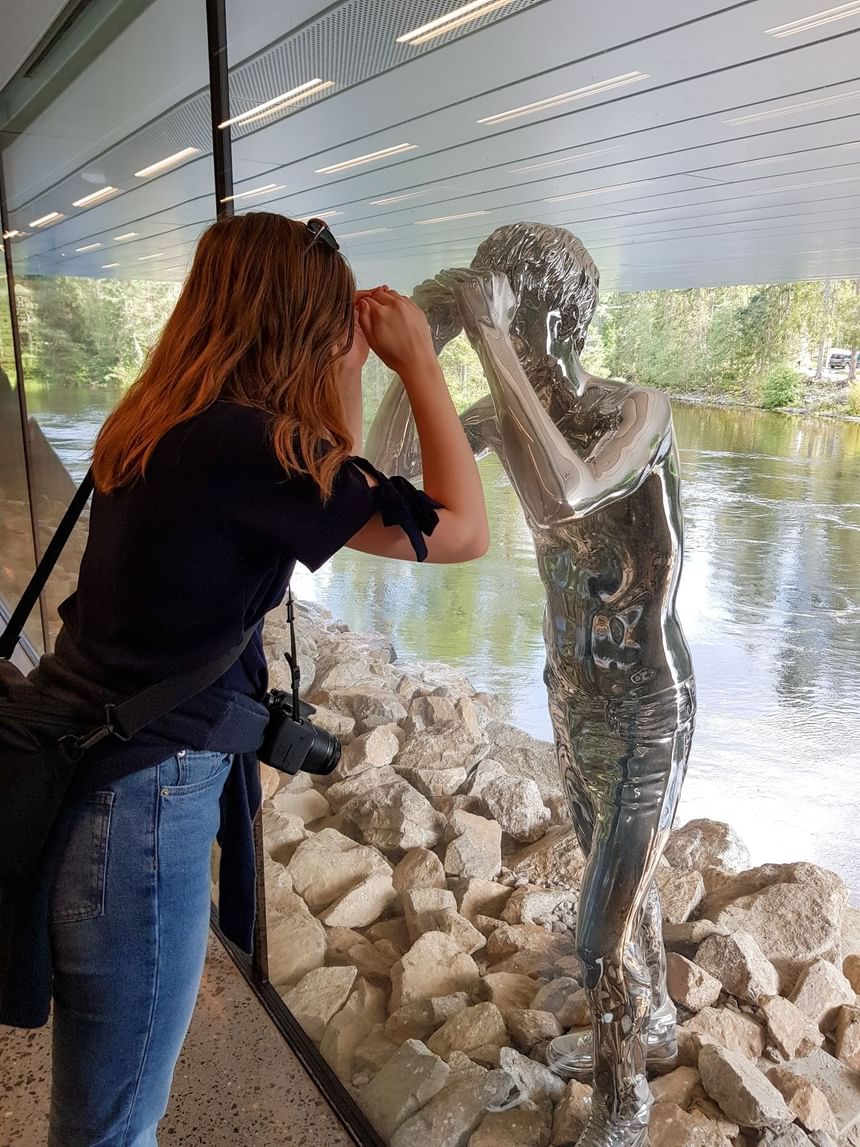 Woman admiring chrome statue of a boy by large window with water views near Tyrifjord Hotel in Norway
