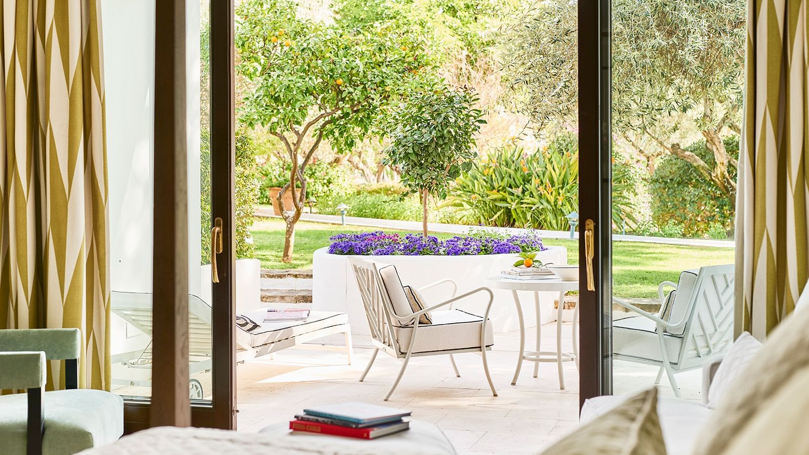 Outdoor patio with a lounge chair and table set by a planter under orange trees at Marbella Club