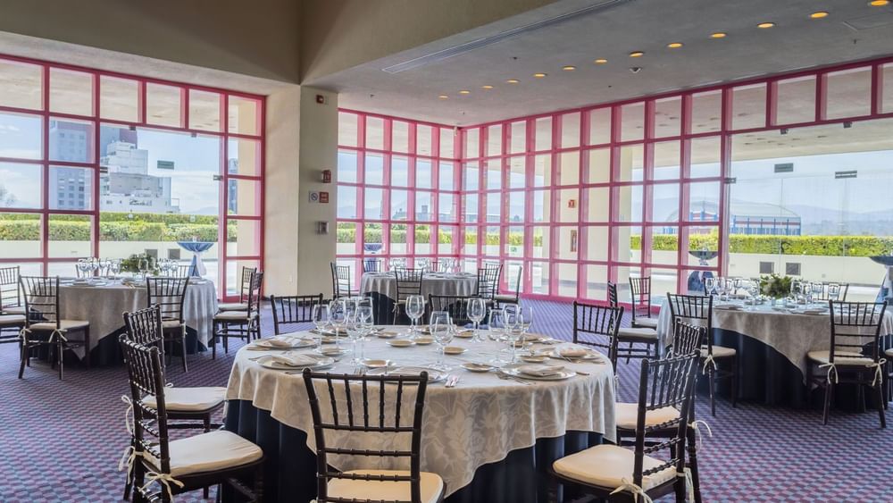 Banquet hall with pink window frames and set tables for a formal event at Camino Real Polanco Mexico
