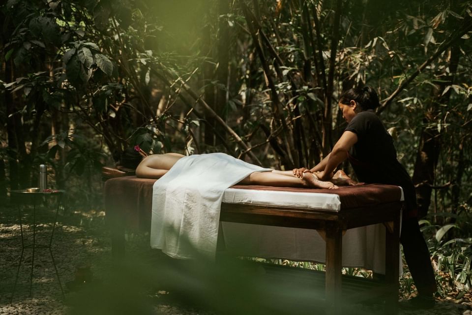 Person enjoying a massage on a wooden table amid lush forest greenery at The Dwarika's Himalayan Wellbeing