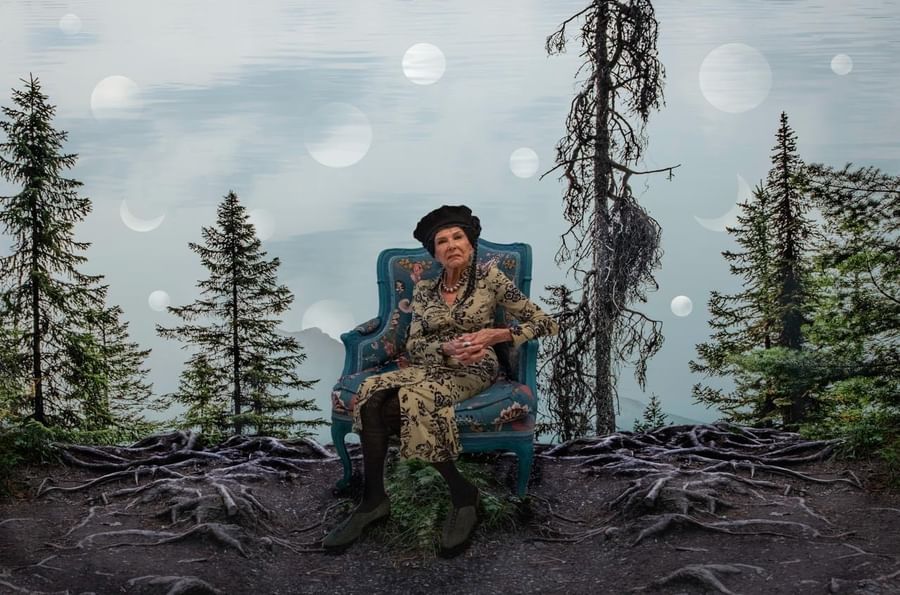 Woman in patterned outfit seated in blue armchair outdoors among evergreen trees at Warwick Le Crystal Montreal
