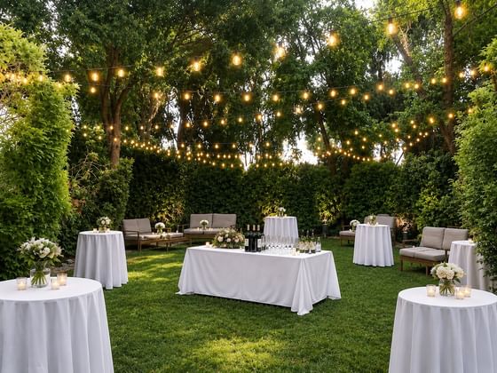 Outdoor garden event space with string lights overhead, white cocktail tables, lounge seating, and wine bar at Cambria Pines Lodge