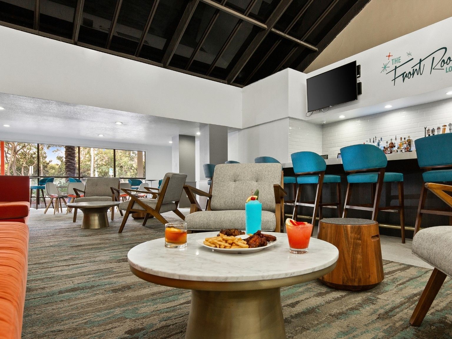 Modern lounge with colorful seating, bar area, and appetizers on a round table at The Anaheim Hotel in Anaheim