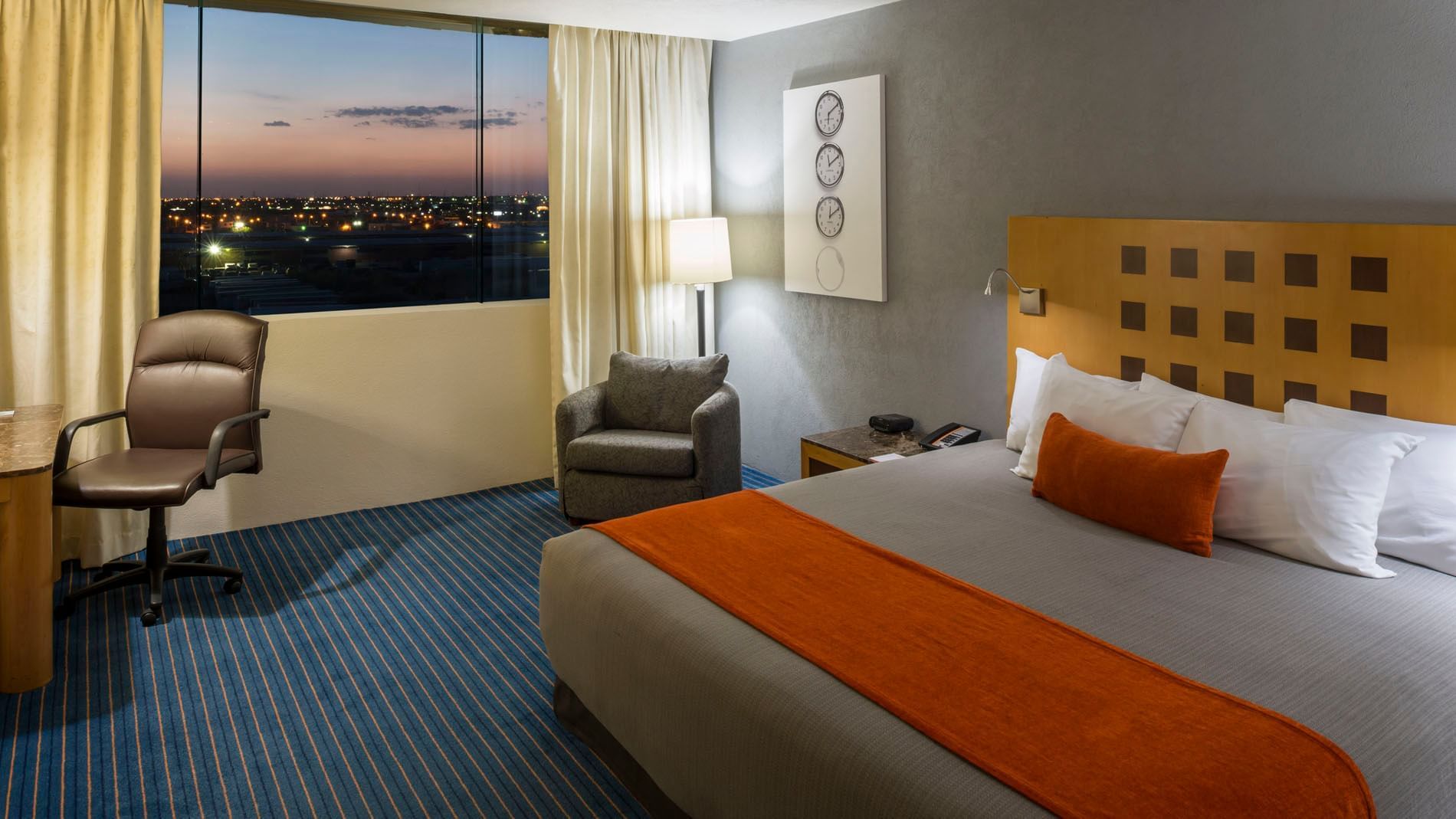 Sunset city view from King Junior Suite featuring a desk chair and a cozy corner armchair at Real Inn Nuevo Laredo