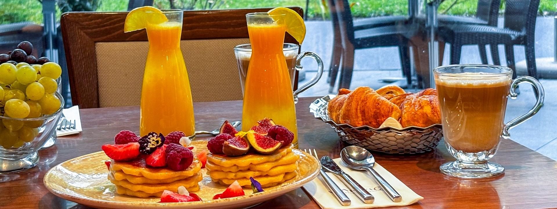 Breakfast table with pancakes, orange juice, croissants, and a latte in Roseraie Room at Warwick Reine Astrid - Lyon