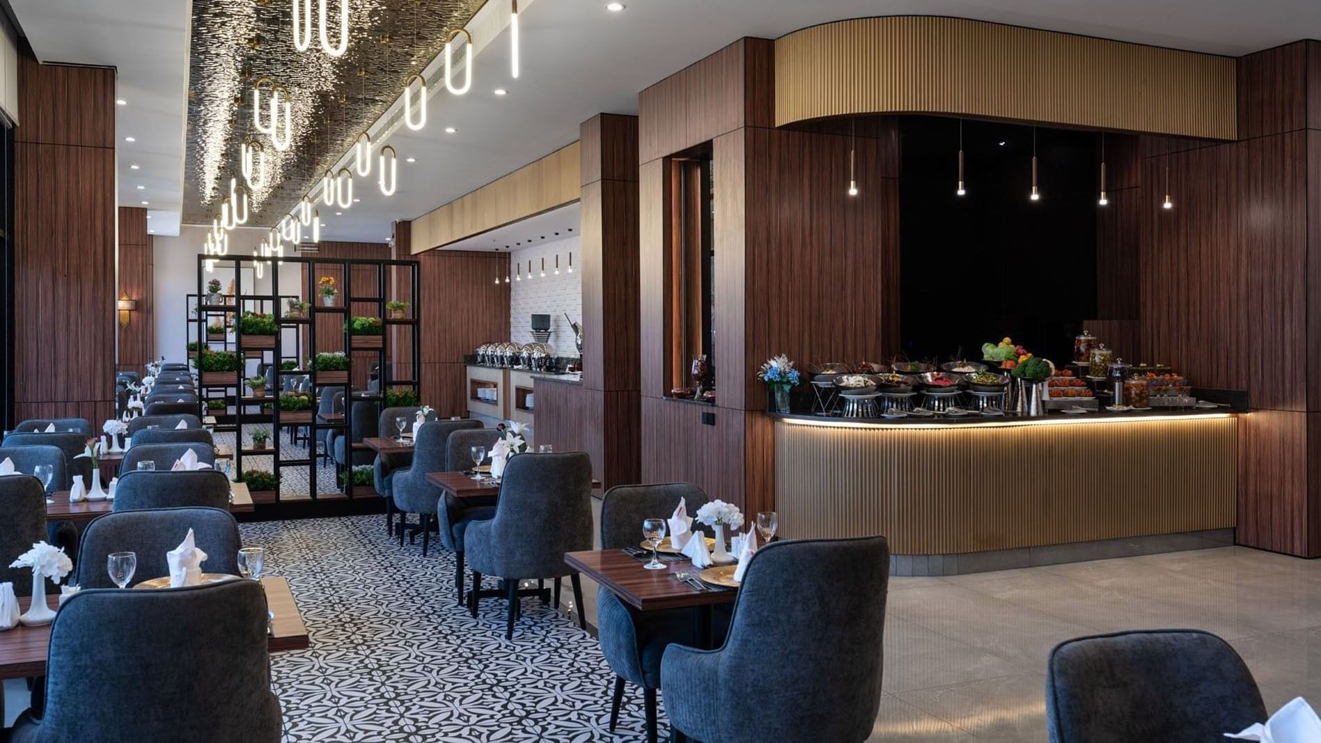 Blue chairs by wooden tables surrounding a patterned floor under oval lights in KVNT at Warwick Al Jubail