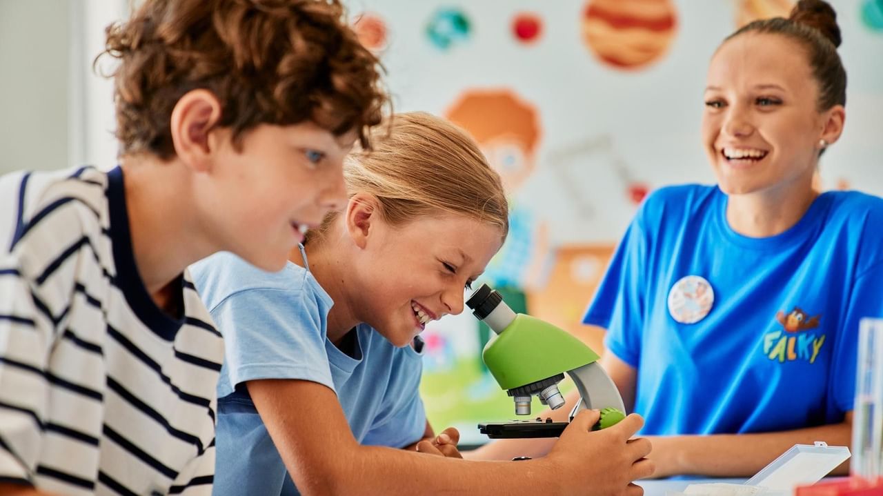 Drei Kinder und eine Erwachsene arbeiten gemeinsam an einem Mikroskop in einem hellen Raum.