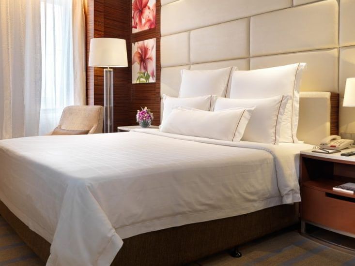 Neatly made king bed with two bedside lamps in Premier Suite with carpeted floors at One World Hotel
