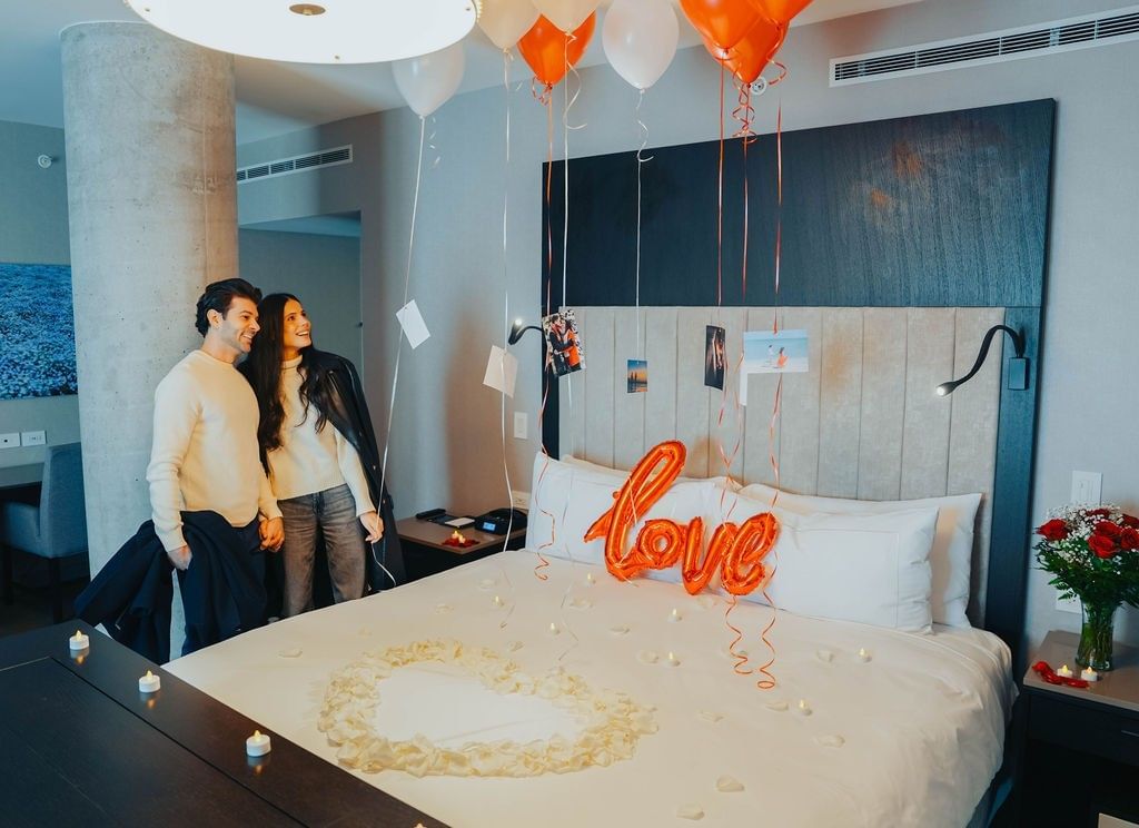 Couple admiring a bed decorated with balloons and photos hanging above at Hotel X Toronto