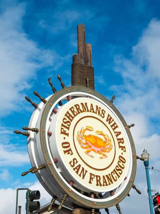 Fisherman's Wharf sign by a wooden mast under a blue sky near Warwick San Francisco