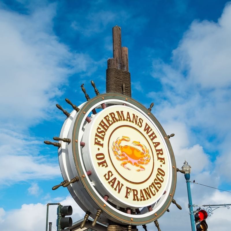 Fisherman's Wharf sign by a wooden mast under a blue sky near Warwick San Francisco