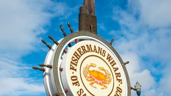Fisherman's Wharf sign by a wooden mast under a blue sky near Warwick San Francisco