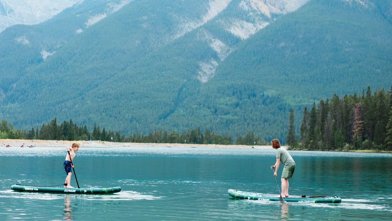Two people paddleboard on a lake in Canmore with the mountains in the background.