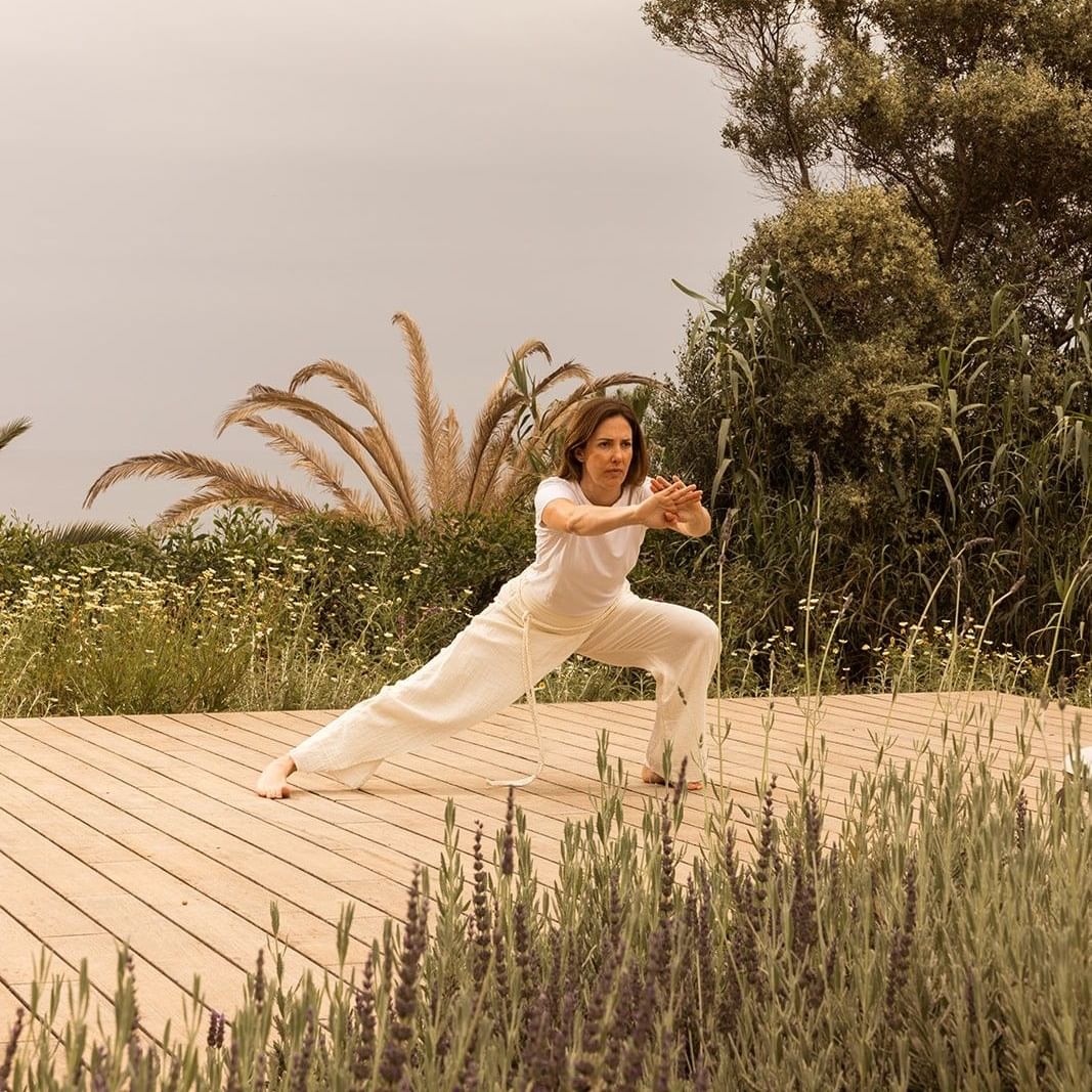 Woman performing yoga pose on wooden deck surrounded by nature at Luminaries in Bloom.