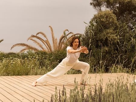 Woman performing yoga pose on wooden deck surrounded by nature at Luminaries in Bloom.