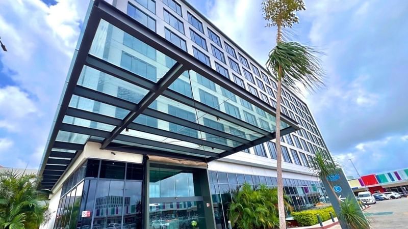 Fiesta Inn Express Cancun Cumbres exterior featuring a striking glass-covered entrance and dark metal framing