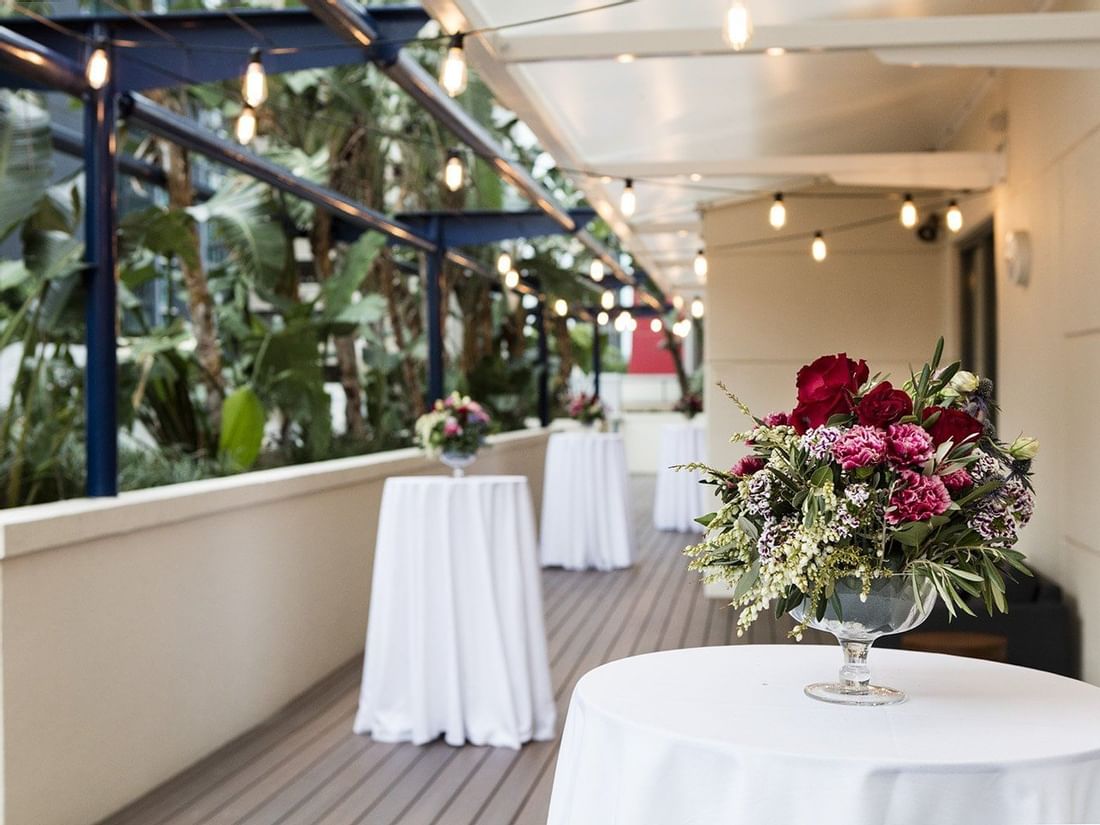Outdoor terrace set up for a cocktail event with white-draped tables, flowers, and string lights at The Sebel Brisbane