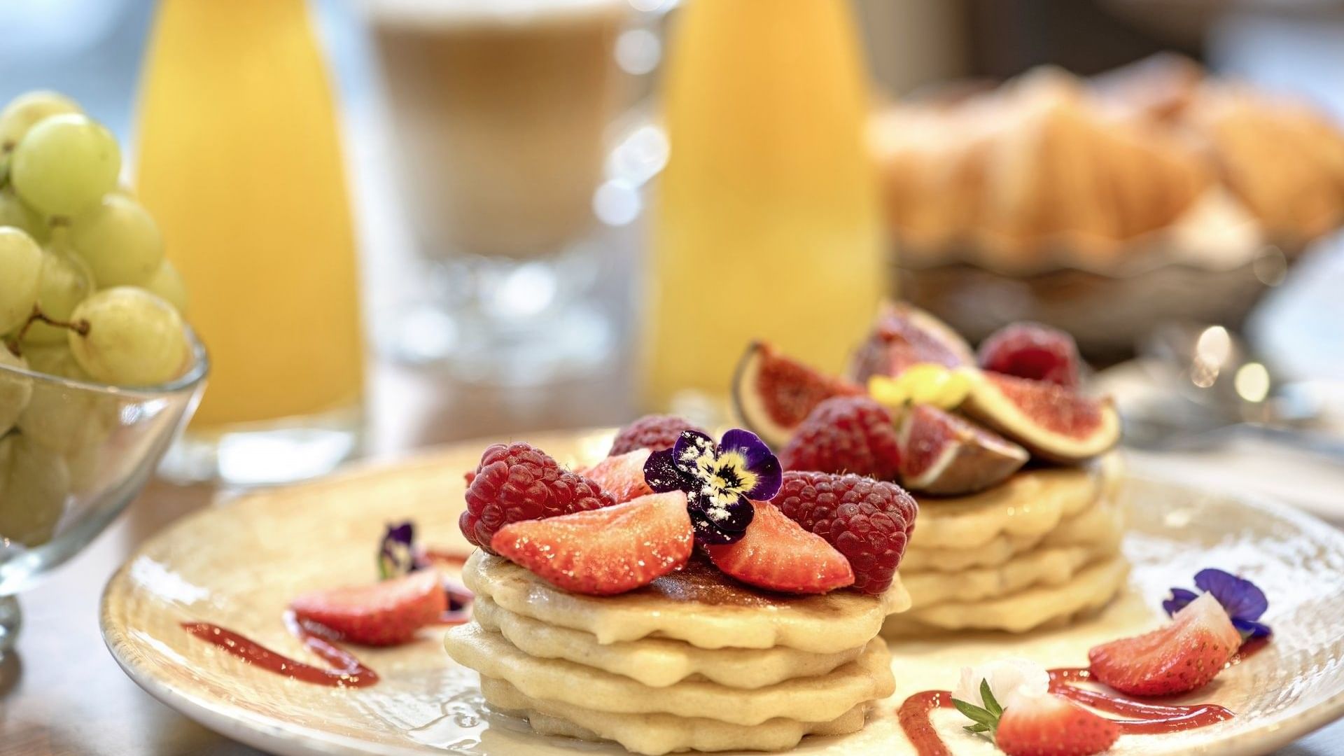 Stacked pancakes topped with fresh figs, berries, and a purple flower in the Roseraie Room at Warwick Reine Astrid - Lyon