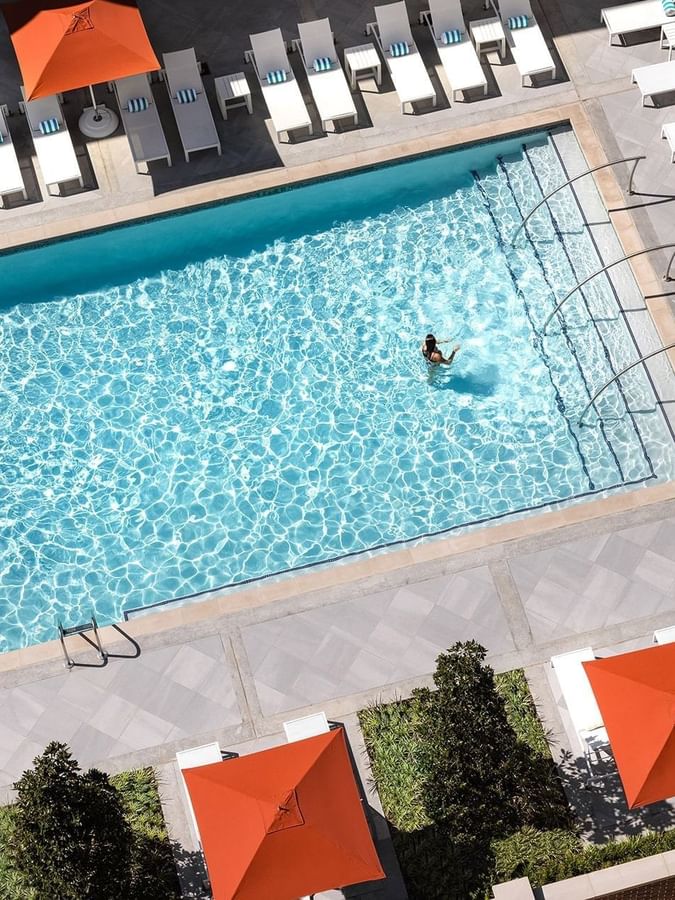 Blue pool by lounge chairs under orange umbrellas surrounding the outdoor deck at Warwick Melrose Dallas