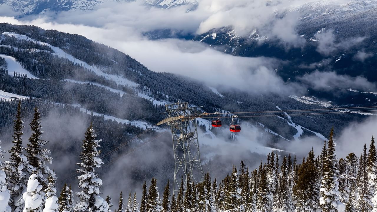 Snow-covered mountains and red gondolas in Whistler surrounded by mist and winter forest near Listel Whistler, a Coast Hotel