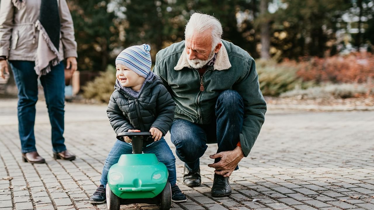 Grandfather kneeling while Grandson rides a toy car