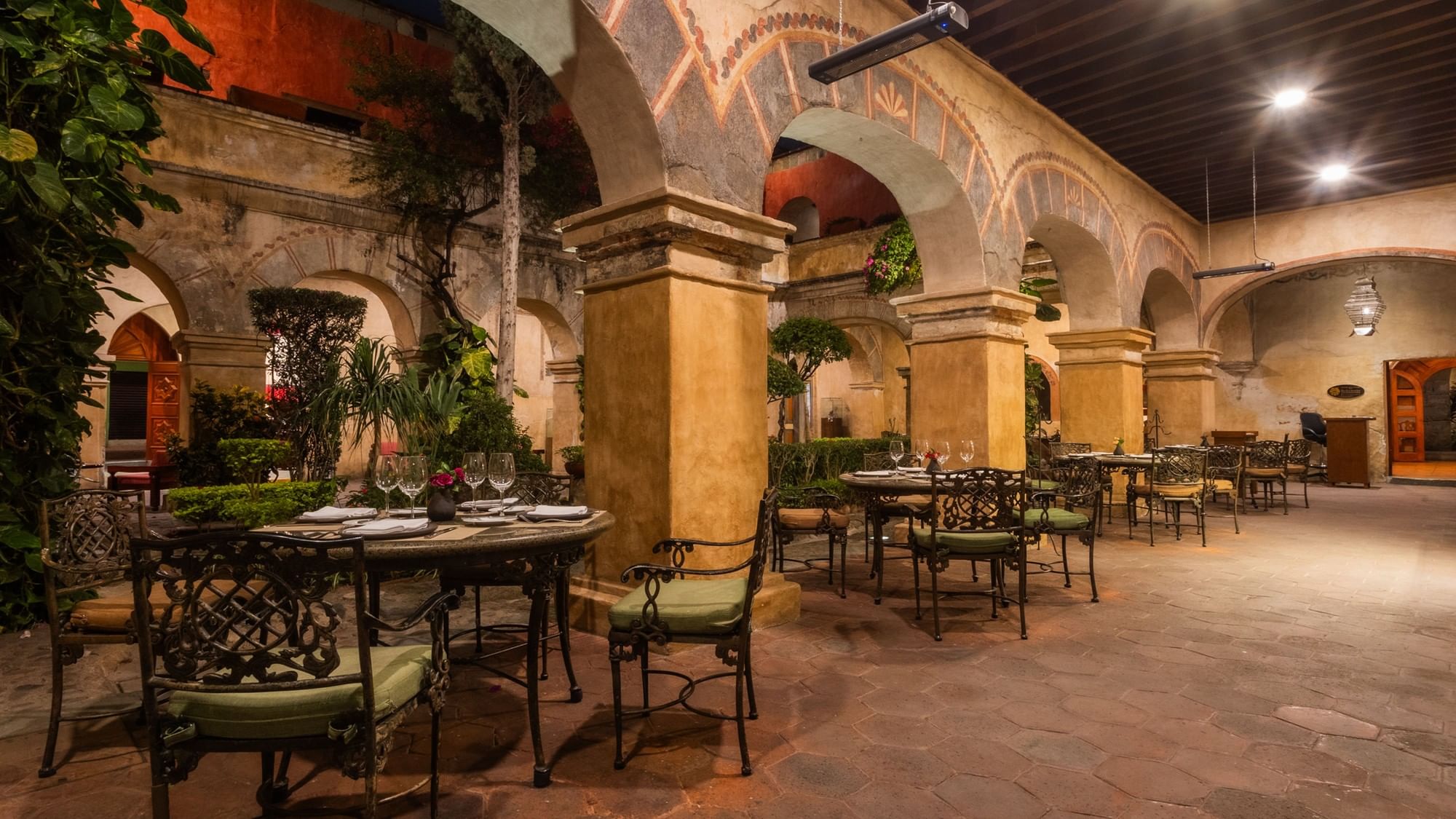 Outdoor hotel dining area with stone arches and green cushioned chairs at Quinta Real Oaxaca